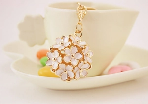 Detail of golden floral sphere keychain featuring white enamel daisy petals and 3D hollow design