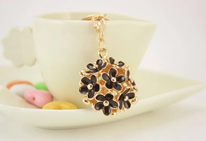 Detail of a gold flower ball keychain with black enamel petals on a coffee cup