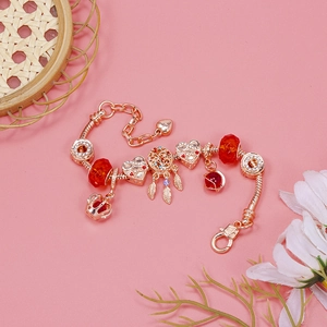 Detailed close-up of a gold charm bracelet featuring red glass beads and crown pendants