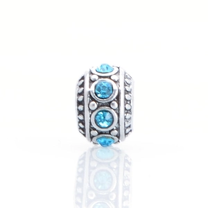Macro view of silver charm bead with sky blue crystal and textured relief detail