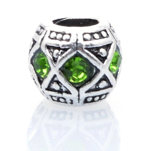 Macro shot of silver charm bead with green rhinestones and geometric triangle cutouts