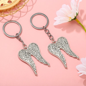 Macro shot of silver angel wing keychains with sparkling rhinestones on pink background