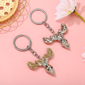 Detail view of two silver reindeer keychains with amber rhinestones on pink background