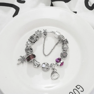 Bracciale con perline argentate, ciondoli viola, palma e pendente a corona su un vassoio