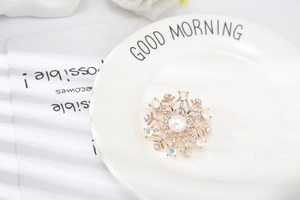 Détail d'une broche flocon de neige avec perle blanche et cristaux colorés sur un plateau