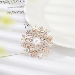 Broche flocon de neige dorée avec perle blanche et cristaux sur une assiette en céramique