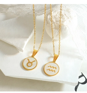 Close-up of golden zodiac pendants with white seashell inlay on a minimalist background
