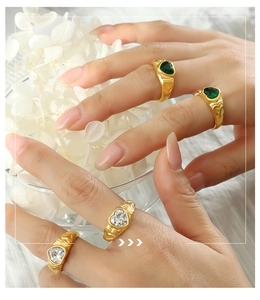 Close-up of gold heart rings with green and clear gemstones on a textured band