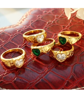 Close-up of gold plated heart rings with white and green stones on leather background