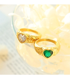 Detail of vintage gold heart rings with white and green stones on a glass rim