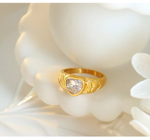 Macro shot of gold-plated ring with heart-shaped stone and hammered texture on white shell
