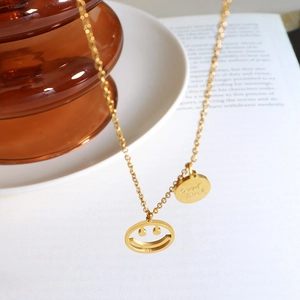 Collar minimalista de oro con colgante de cara sonriente y medalla Good Luck en plato blanco
