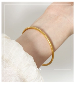 Close-up of minimalist matte gold round tube bangle on wrist with white sleeve