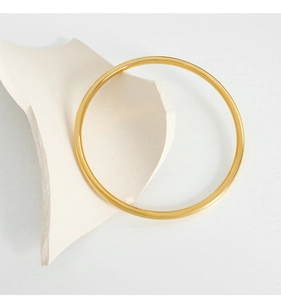 Artistic close-up of a minimalist gold-plated titanium steel bangle on paper