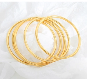Macro shot of seven thin stackable gold-finished titanium steel bangles on white paper