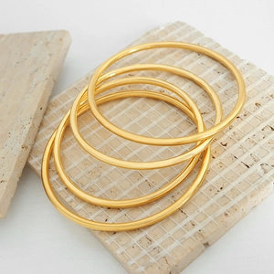 Set of four minimalist gold-plated titanium steel stackable bangles on a textured stone block