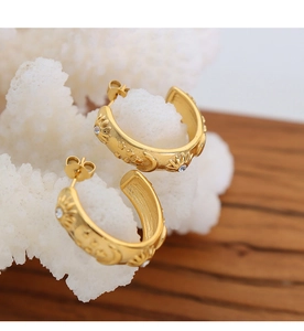 Detail of C-shaped gold-plated steel earrings with sun moon relief and sparkling zircons
