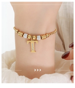 Detailopname van een gouden kralenarmband met een T-letter hanger voorzien van kristallen
