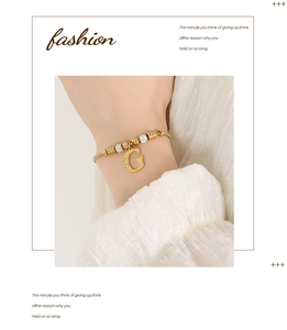 Detail van een gouden armband met een strass letter G-hanger en kralen bedeltjes