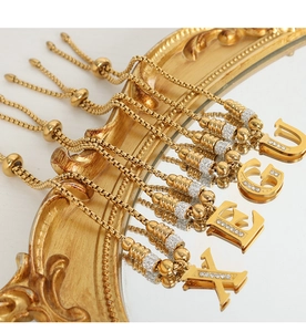 Detailopname van gouden letterhangers U G E X met micro-pave zirkoon en box kettingen