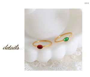 Macro detail of gold rings with oval red and green gemstones on white ceramic tray
