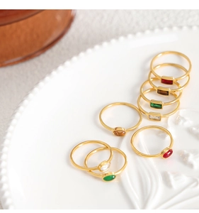 Detail shot of slim gold titanium rings with colorful glass stones on a white ceramic plate