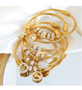 Detalle de pulseras de serpiente doradas con varios dijes de circón sobre seda blanca