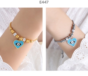Detail view of 18K gold and silver beaded bracelets featuring blue enamel evil eye hearts