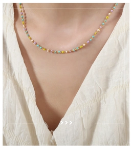Primer plano de collar dorado con perlas de esmalte de colores en camisa blanca