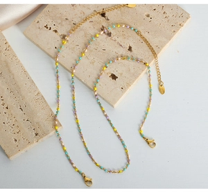 Detalle de cadena de acero inoxidable dorado con perlas de colores sobre piedra