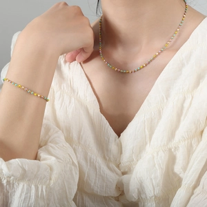 Conjunto de collar y pulsera de cuentas de colores dorados en modelo con camisa blanca
