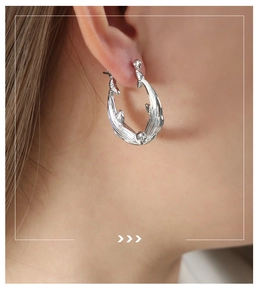 Gros plan d'une boucle d'oreille créole argentée au design de métal liquide irrégulier