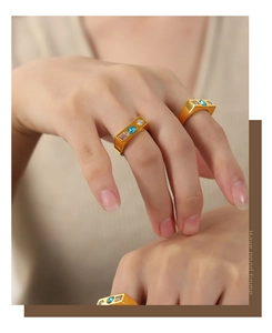 Dettaglio macro dell'anello a fascia quadrata dorata con pietre rosa, blu e bianche