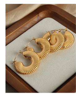 Detail van gouden croissant-oorringen met geribbelde textuur op een beige dienblad
