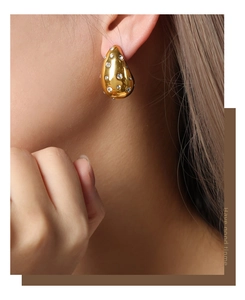 Close-up of golden teardrop hollow earrings with inlaid rhinestones on model's ear