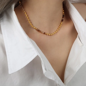 Collar minimalista con cuentas doradas y piedra natural marrón en una modelo