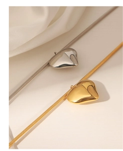 Nahaufnahme von Gold- und Silber-Herzanhängern mit Schlangenkette auf seidigem Stoff