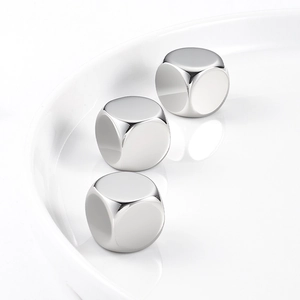 Three pieces of polished stainless steel ice cubes with rounded edges on white plate