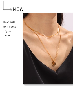 Close-up of double layered gold snake chain and bead necklace with tiger eye stone pendant