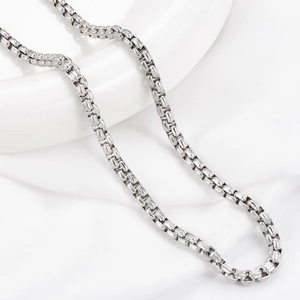 Detail shot of silver stainless steel box chain necklace on white ceramic and fabric