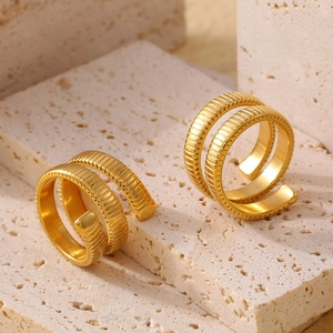 Anillos Tubogas dorados de doble capa con textura ranurada sobre piedra beige