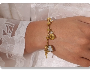 Detail of a gold charm bracelet with star and heart pendants worn on a female wrist