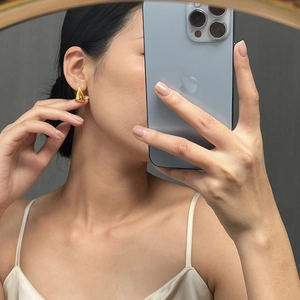 Close-up of golden teardrop earrings in polished titanium steel on model's ear