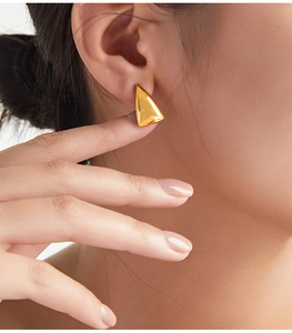 Close-up of polished gold triangular geometric stud earring worn by a model