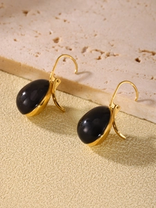 Detail of elegant black resin teardrop earrings set in gold base on stone texture