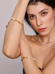 Dettaglio di bracciali con perle barocche e orecchini d'oro indossati da una modella