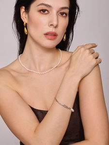 Primo piano di un bracciale con perle barocche e orecchini a goccia dorati su modella