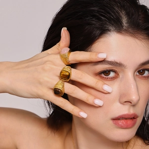 Gold-toned rings set with tiger eye and pink crystal featuring woven metal textures