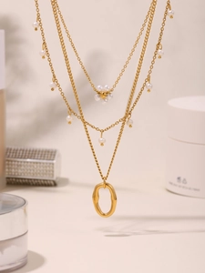 Dettaglio di collana dorata multistrato con perle e pendente ovale su uno sfondo beige