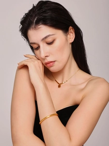 Detail of a gold-plated circular bangle and minimalist square pendant necklace on a model